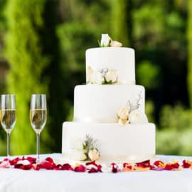 Modern 3-tier white wedding cake with flora decoration made by Ariston Confectionery, and two glasses of champagne.