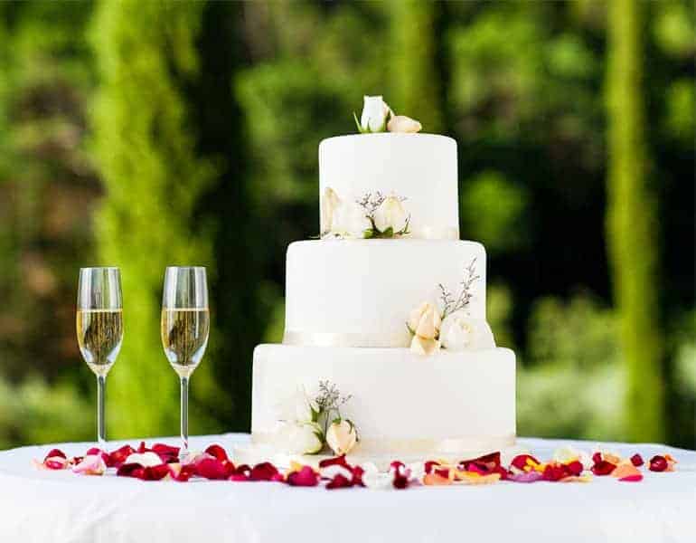 Modern 3-tier white wedding cake with flora decoration made by Ariston Confectionery, and two glasses of champagne.
