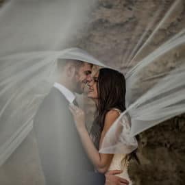 A couple in intimate moments under white lace, during a wedding photoshoot by Photo Bella Photography.
