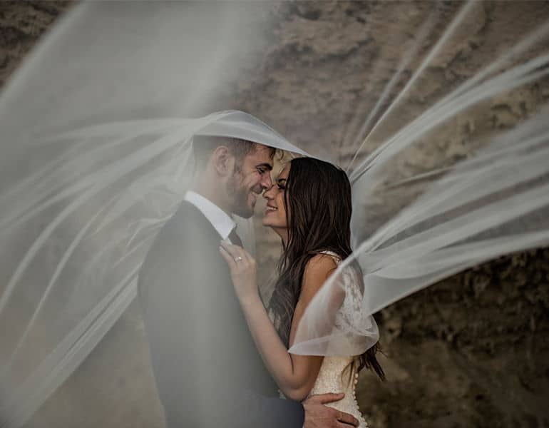A couple in intimate moments under white lace, during a wedding photoshoot by Photo Bella Photography.